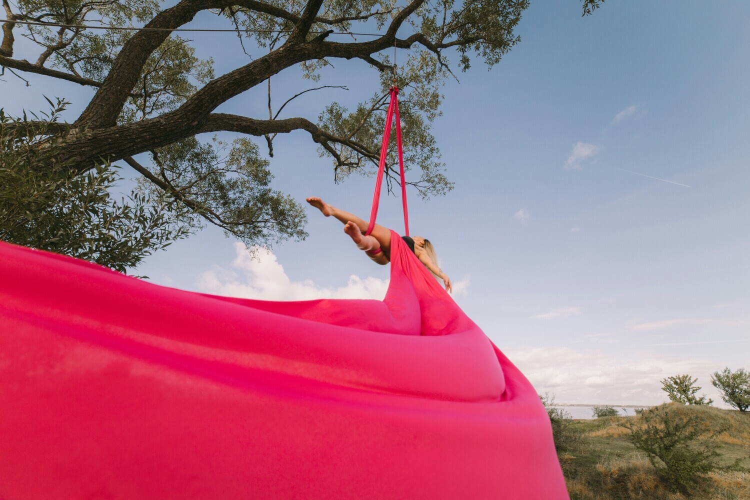 Red fabric extending between body, tree and landscape