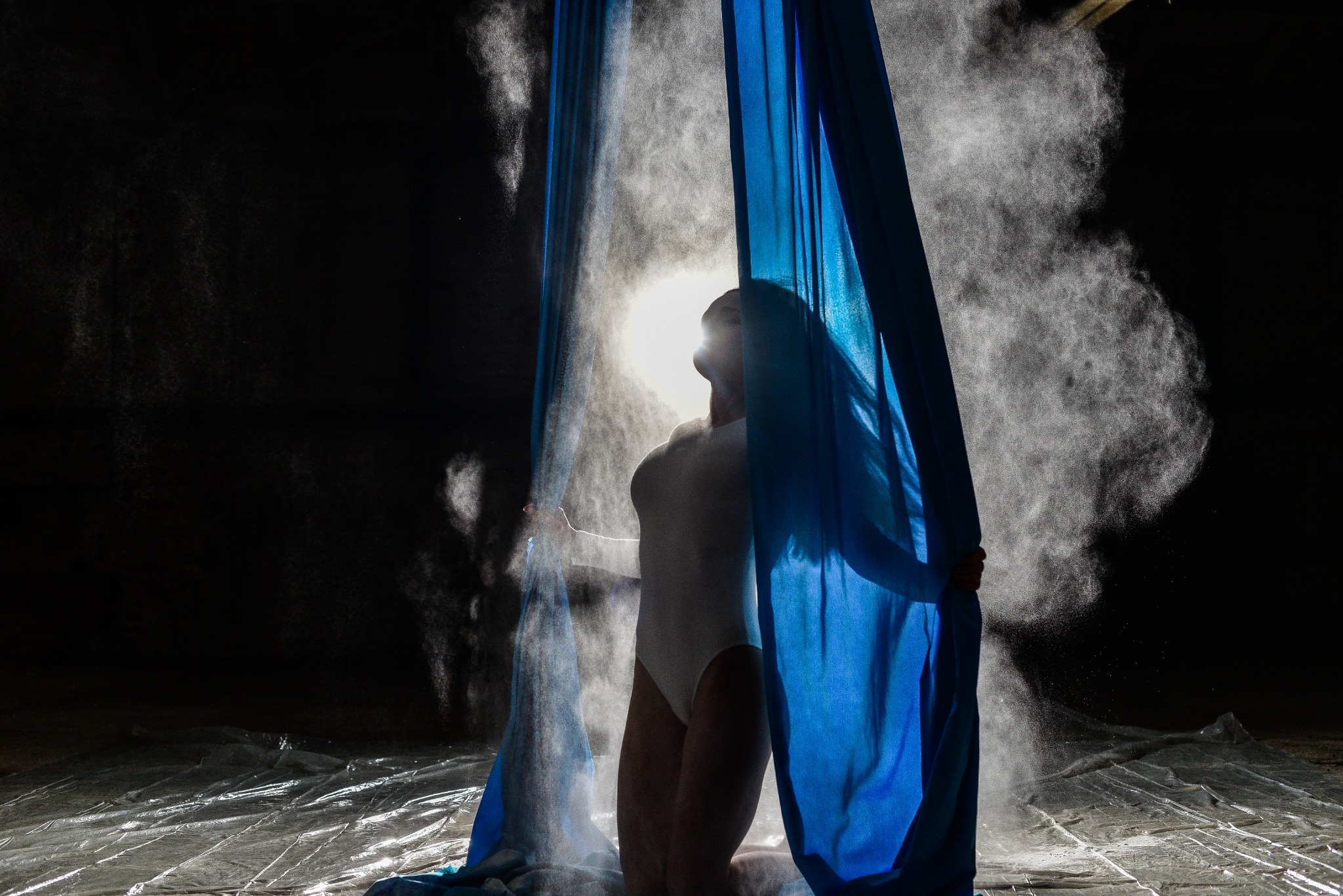 Body behind blue fabric in a cloud of flour